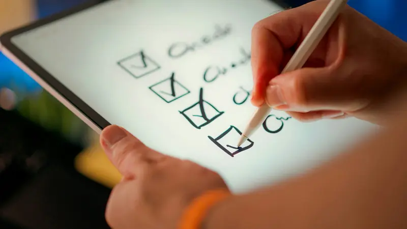 A hand uses a stylus to tick boxes on a handwritten checklist on a tablet screen