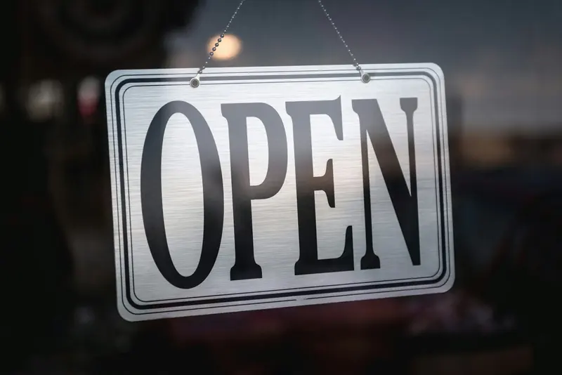 A plain metal OPEN sign hanging on a shop glass door