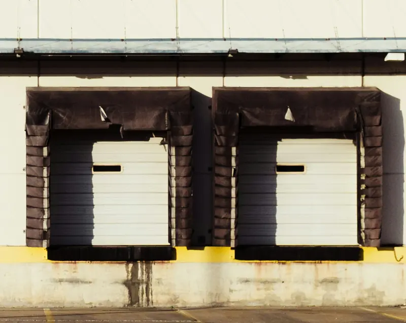 Two closed loading dock doors with dark dock shelters on a cream warehouse wall above a yellow painted ledge