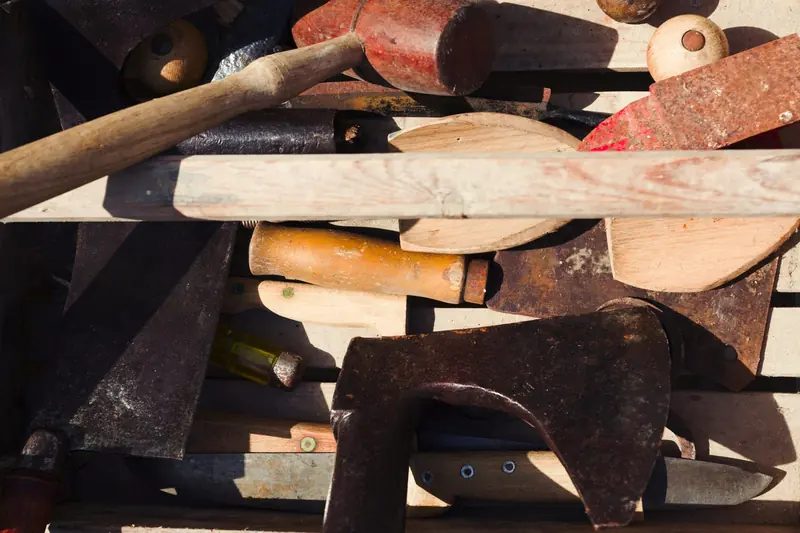 A top down pile of old rusty hand tools including a hammer, saws and an axe in sunlight