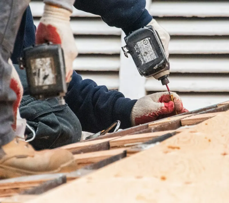 Gloved hands with cordless drills fastening roof decking