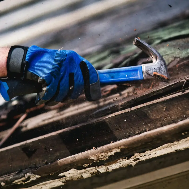 Gloved hand with a hammer tearing off old roofing boards
