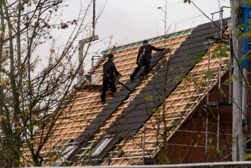 Two roofers installing shingles on a steep roof, seen from a distance
